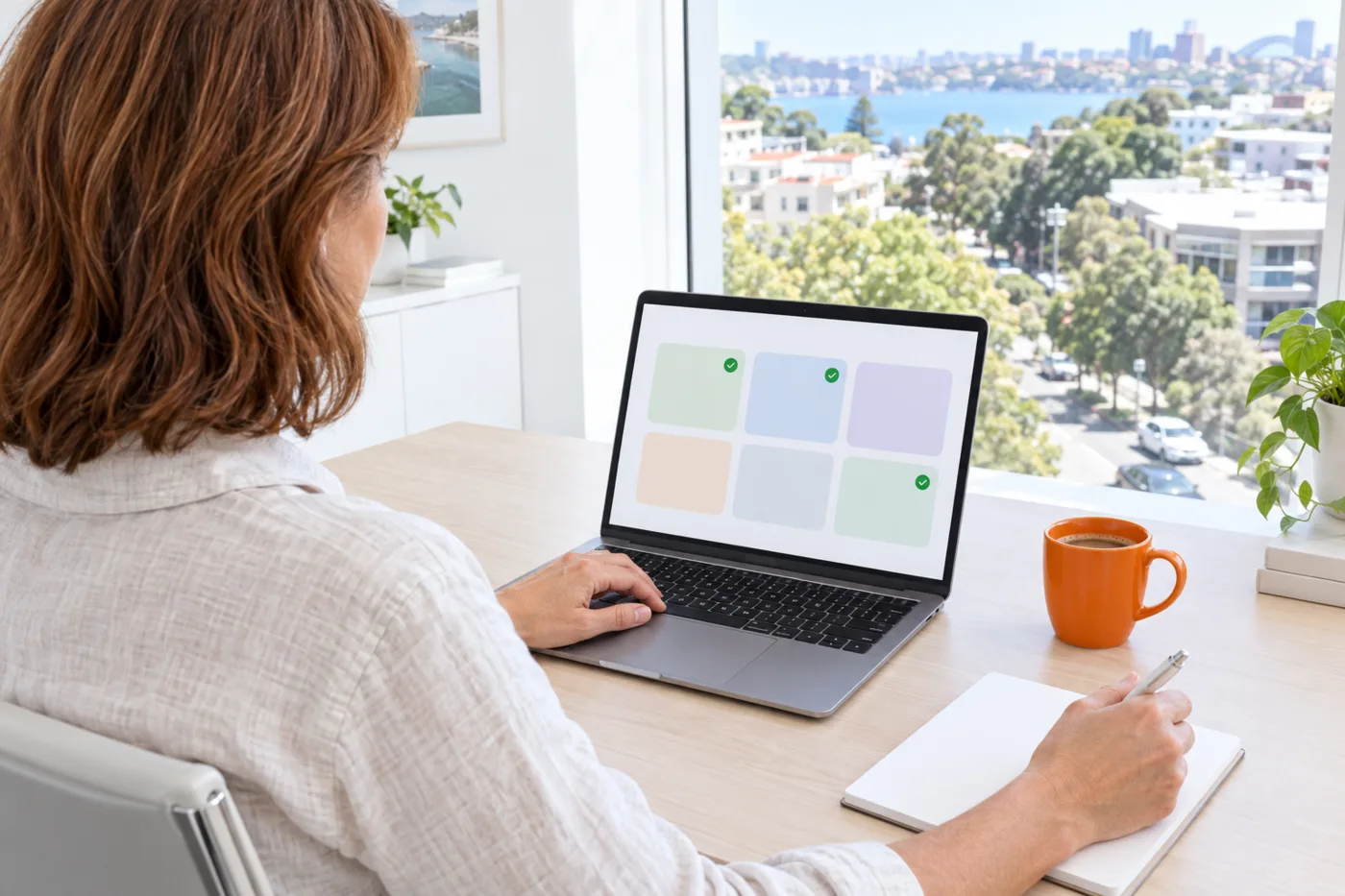 Over-the-shoulder view of a Sydney business owner comparing a shortlist of agencies on her laptop, with a notepad and an orange coffee cup on the desk