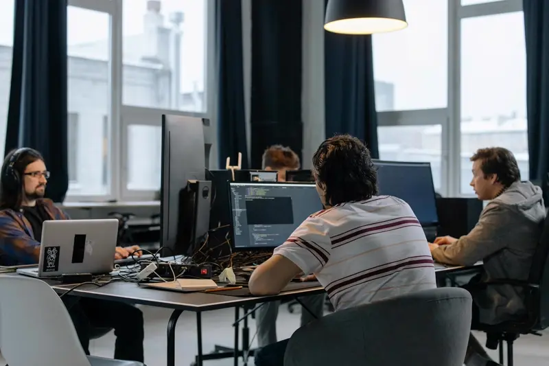 A web design and development team working together at desks in a bright studio, reviewing code and layouts on screen