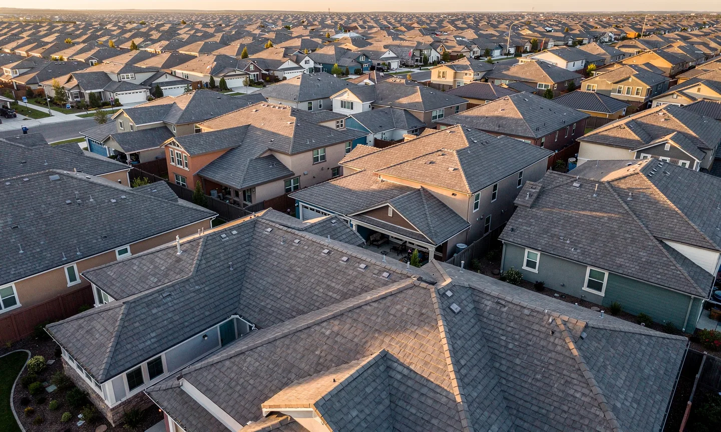 Aerial view of a suburban neighbourhood of asphalt shingle rooftops photographed at golden hour